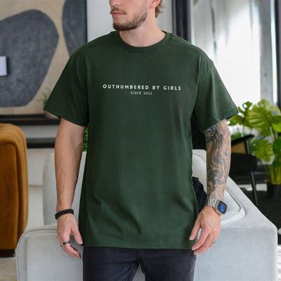 Man wearing an ivory personalized dad of girls shirt printed with Outnumbered by Girls Since 2023 in minimalist text