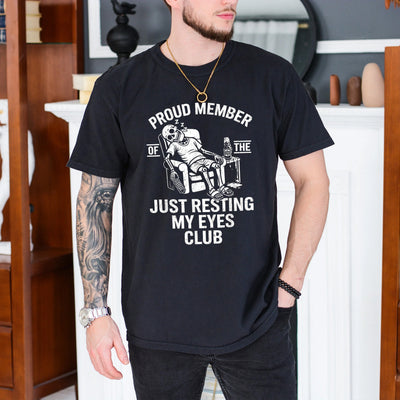 Black unisex t-shirt with a skeleton napping in a recliner holding a remote, just resting my eyes club funny dad design