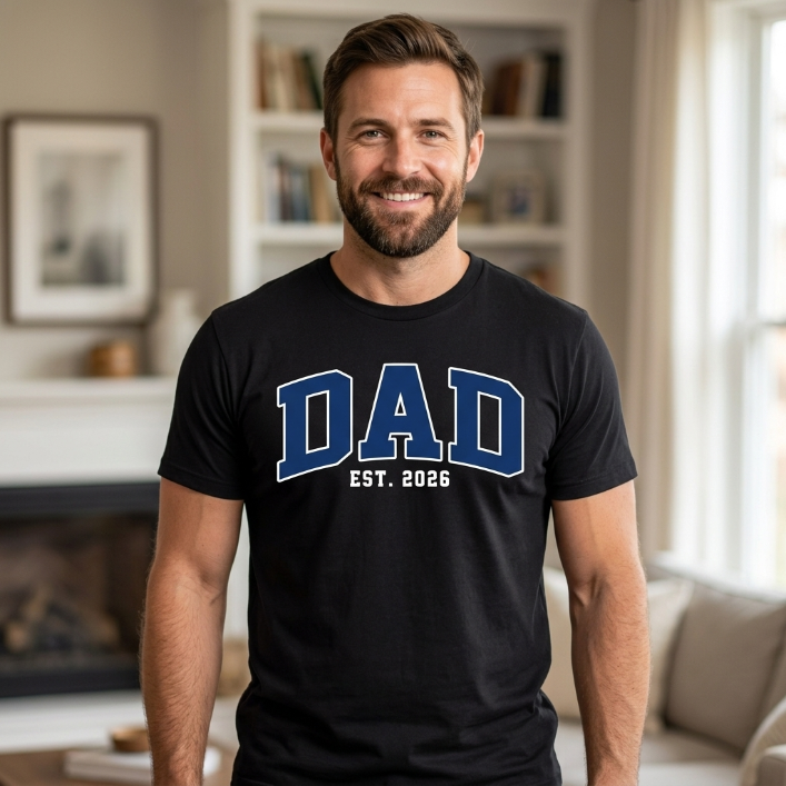 Black unisex t-shirt with bold retro collegiate lettering reading DAD Est. 2026 in navy blue and white