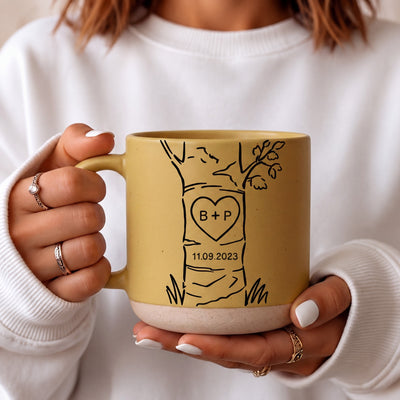 Personalized anniversary mug set with custom initials and date inside a carved heart on a tree illustration, cream and blue coarse ceramic