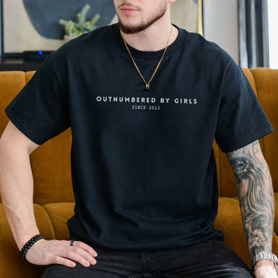 Man wearing an ivory personalized dad of girls shirt printed with Outnumbered by Girls Since 2023 in minimalist text